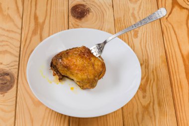 Taze pişmiş tavuk budu kemiğe saplanmış derisi kırsal bir masada beyaz bir tabağa saplanmış.