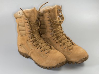 Bir çift su geçirmez yalıtımlı bej savaş botu. Gri arka planda ayakkabı bağcıkları var.