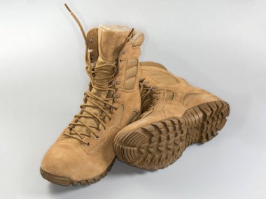 Bir çift su geçirmez yalıtımlı bej savaş botu. Gri arka planda ayakkabı bağcıkları var.