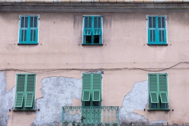 Eski üç katlı binanın ön cephesinin üst kısmında pencereleri yeşil ahşap kapaklı dış panjurlar ve bulutlu bir günde ikinci katta bir balkon var.