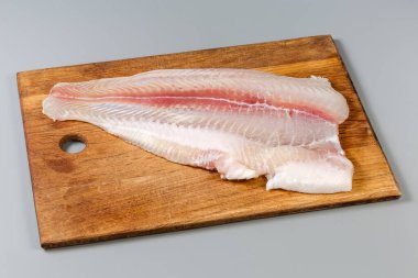 Defrosted fillet of the Pangasius, also known as basa fish on a big wooden cutting board on gray background clipart