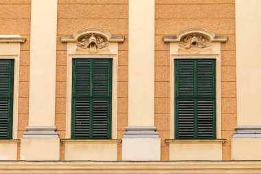 Kapalı ahşap kepenkleri olan pencereler kapalı bir günde sarı duvarda yeşile boyanmış.