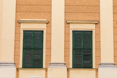 Kapalı ahşap panjurlu iki pencere, kapalı bir günde sarı duvarda yeşile boyanmış.