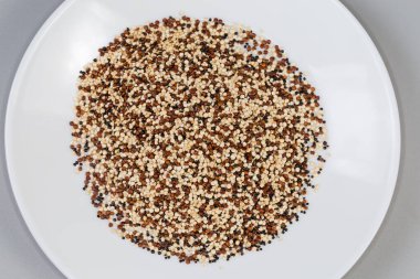 Heap of the mix of raw black, red and white quinoa seeds on a white dish, top view on a gray background clipart