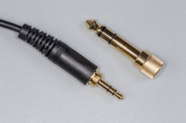Analog ses stereo kablosunun kenarındaki mini Jack 'i ve metal vida adaptörünü altın renkli Jack' e tak. Gri bir yüzeye yakın çekim yap.