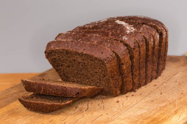 Çavdar ekmeğinden gelen kahverengi ekmeğin dilimlenmiş dikdörtgen somunu ve tahta kesme tahtasının üzerinde buğday unu, seçici bir odak noktasında ön manzara.