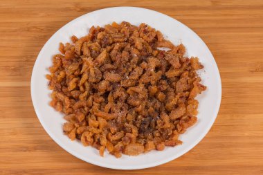 Ördek yağı ve deri dilimlerinden elde edilen çıtırtılar, daha sonra tuzlu ve biberli baharatlarla tatlandırılırken, ahşap bir yüzeyde beyaz bir tabakta servis ediliyor.