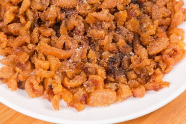 Ördek yağı ve deri dilimlerinden elde edilen çıtırtılar uzun süre eridikten sonra tuzlu ve biberli beyaz bir tabakta, yakın çekim parçasıyla tatlandırılmış.