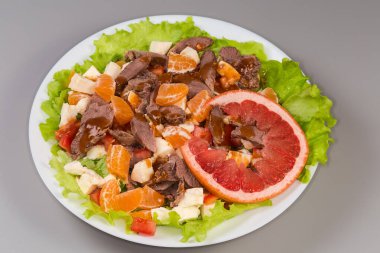 Haşlanmış ördek etinden yapılmış salata, doğranmış mozzarella, farklı taze narenciye, sebze ve yeşillikler gri arka planda büyük beyaz bir tabakta.