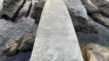 Kıyı kayaları, yaya köprüsü, deniz yüzeyi ve sabah gökyüzü.