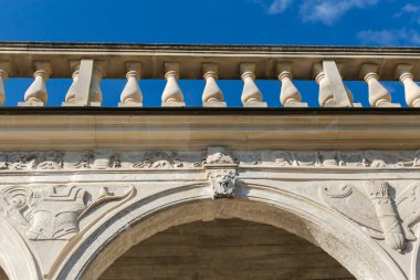 Güneşli bir günde ortaçağ şatosunun tepesinde, açık gökyüzüne karşı alttan bakan, oyulmuş hafif kumtaşından yapılmış eski kemerli galerinin üst kısmı.