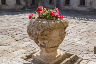 Ortaçağ şatosunun iç avlusunda çiçek açan kırmızı petunyalı eski bir taş bahçe vazosu güneşli bir günde antik taş levhalarla kaplanmış.