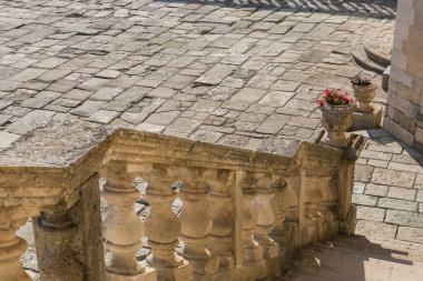 Güneşli bir günde ortaçağ şatosunda kumtaşından vazolar ve eski taş levhalarla döşenmiş avluya bakan eski merdiven korkulukları.