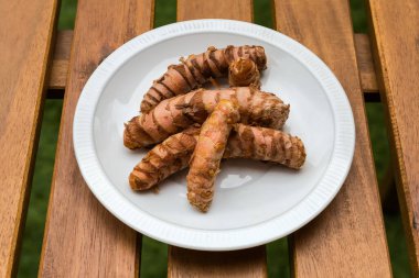 Terastaki ahşap bir masadaki beyaz tabakta taze zerdeçal rizomları.