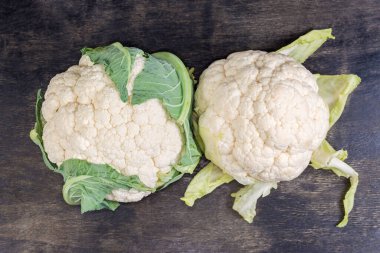 İki taze çiğ karnabahar başı siyah bir yüzeye yakın bir yaprak ile, üst görünüm