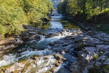 Çok katmanlı şelale, sonbahar güneşli bir günde, dağlık bir nehirde, yamaçların arasında, panoramik manzaralı.