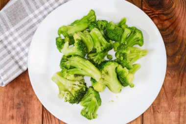 Brokoliden taze kaynamış parçalar, beyaz tabağın üzerinde, kırsal bir masada, en üstte yakın plan.