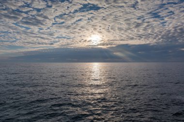 Gökyüzünün bir bölümü altokümülüs bulutlarıyla denizin su yüzeyinde güneşli bir yol ve sonbahar sabahı ufuk çizgisinde uzak fırtına bulutları.