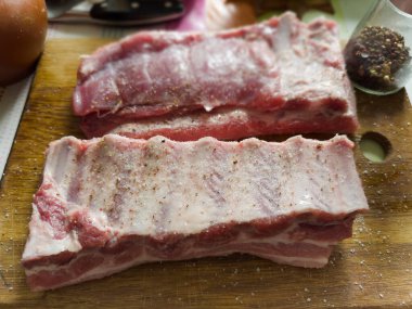 Ahşap kesme tahtasına tuz ve baharat serpiştirilmiş çiğ domuz pirzolası serpiştirilmiş, seçici odaklı yakın plan.