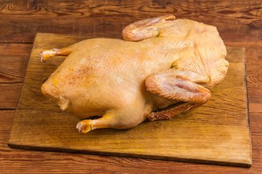 Köhne bir masada ahşap bir kesme tahtasının üzerinde evcil ördek leşi, ördeğin arkasından manzara.