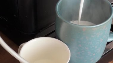 Otomatik kahve makinesinden mavi fincana donmuş süt dökülüyor.