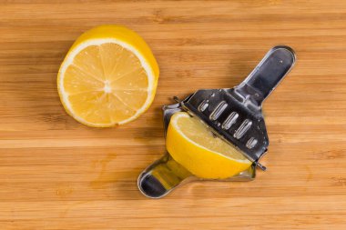 İçinde taze limon dilimi ve yanında da dilimlenmiş limon bulunan küçük basın maşası şeklinde paslanmaz çelik limon sıkıcıyı aç.