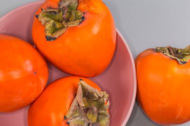 Pembe kasede olgun organik hurma meyveleri ve yanında bir meyve duruyor. Gri arka plandaki parçanın en üst görüntüsü.