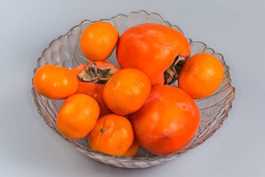 Gri bir arka planda cam meyve kasesinde olgun organik meyve ve mandalina.