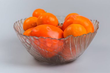 Olgun organik hurma ağaçları ve mandalinalar cam meyve kasesinde, yakın plan gri arka planda.