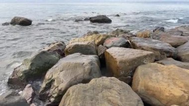 Kıyıya yakın taşlar bulutlu bir sabahta deniz suyuyla yıkanır.