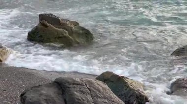 Kumlu sahildeki taşlar bulutlu deniz suyuyla yıkanır.