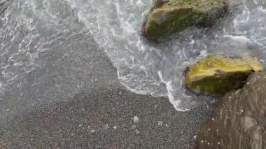 Kumlu sahildeki taşlar bulutlu deniz suyuyla yıkanır.