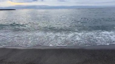 Kara kumlu sahilde, bulutlu bir sabah sörf.