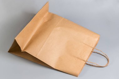 Düz tabanlı boş tek kullanımlık çanta, açık kahverengi, ağartılmamış kağıt ve gri arka planda bükülmüş kağıt tutamaklar.