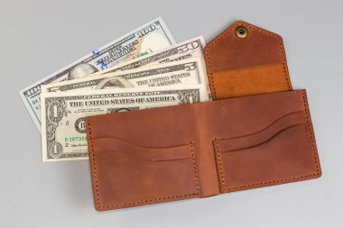 Birkaç farklı banknotta klasik tarzda katlanmış kahverengi deri cüzdan, gri arka planda üst görünüm.
