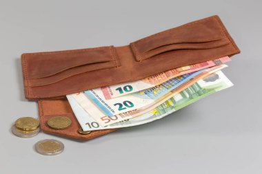 Klasik tarzda katlanmış kahverengi deri cüzdan içinde birkaç banknot ve gri arka planda paralar, seçici odak noktasında ön plan yakın çekim