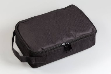 Fermuarlı, küçük, siyah, yumuşak, dikdörtgen bir çanta ve gri bir arka planda, tekstil kayışı şeklinde sabitlenmiş.