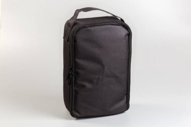 Fermuarlı, küçük, siyah, yumuşak, dikdörtgen bir çanta ve gri bir zemin üzerinde duran tekstil kayışı şeklinde sabitlenmiş.