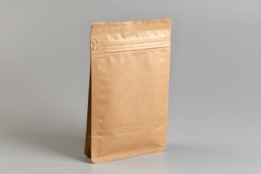 Kuru gıda ürünlerinin tokalı küçük açık kahverengi paket çantası gri bir arka planda duruyor.