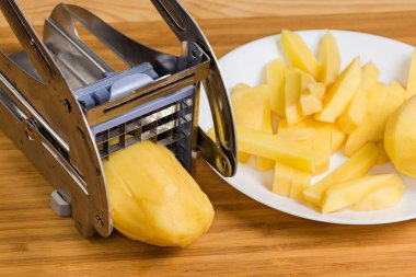 Patates kızartması için patatesi kesmek için elle paslanmaz çelik dilimleyici. Kırsal bir masada dilimlenmiş çiğ patates, yakın plan.
