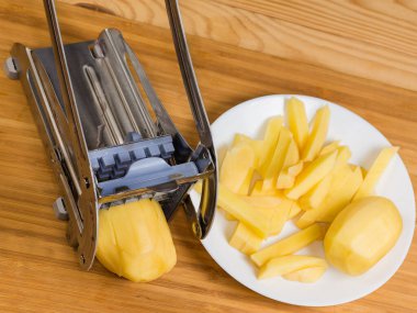Patates kızartması için patatesi kesmek için elle paslanmaz çelik dilimleyici. Kırsal bir masada dilimlenen çiğ patates, üst kısmı yakın plan.