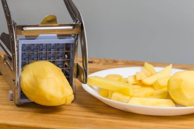 Patates kızartması için patatesi kesmek için elle paslanmaz çelik dilimleyici. Kırsal bir masada çiğ patates dilimleme sırasında.