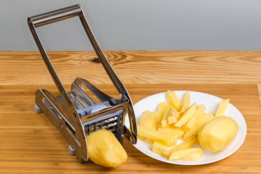 Patates kızartması için patatesi kesmek için elle paslanmaz çelik dilimleyici. Kırsal bir masada dilimlenmiş çiğ patates.