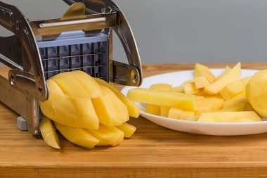 Patates kızartması için çiğ patates dilimleme elle paslanmaz çelik dilimleyici ile kesme tahtasındaki patatesi kesmek için seçici odak noktasındaki parçanın ön görüntüsü.