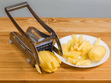 Patates kızartması için patatesi kesmek için elle paslanmaz çelik dilimleyici. Kırsal bir masada dilimlenmiş çiğ patates.