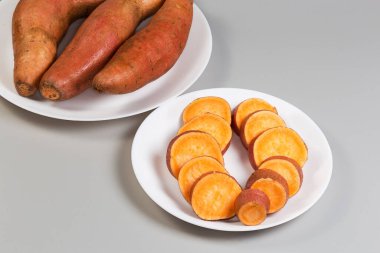 Çiğ patates yumrusu. Derisi beyaz tabakta dilimlenmiş. Gri arka plandaki diğer büyük tabağın tümüne karşı.