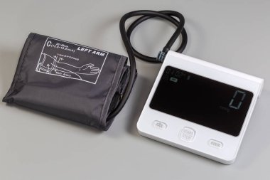 Elektronik otomatik sphygmomanometre, ölçüm ünitesi ve şişme manşet gri arka planda yatar.