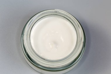Küçük cam kavanozda beyaz kozmetik krem. Gri bir yüzey üzerinde kapağı yok. Üst manzara.