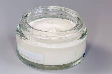 Özel cam kavanozda beyaz kozmetik krem gri arka planda vida kapağı çıkarılmış.