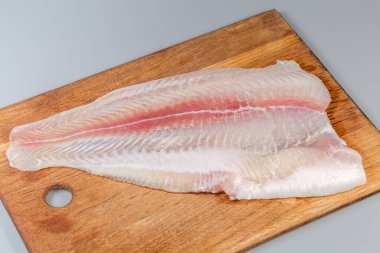 Pangasius 'un çözülmüş filetosu. Gri arka planda büyük bir ahşap kesim tahtasındaki basa balığı olarak da bilinir.